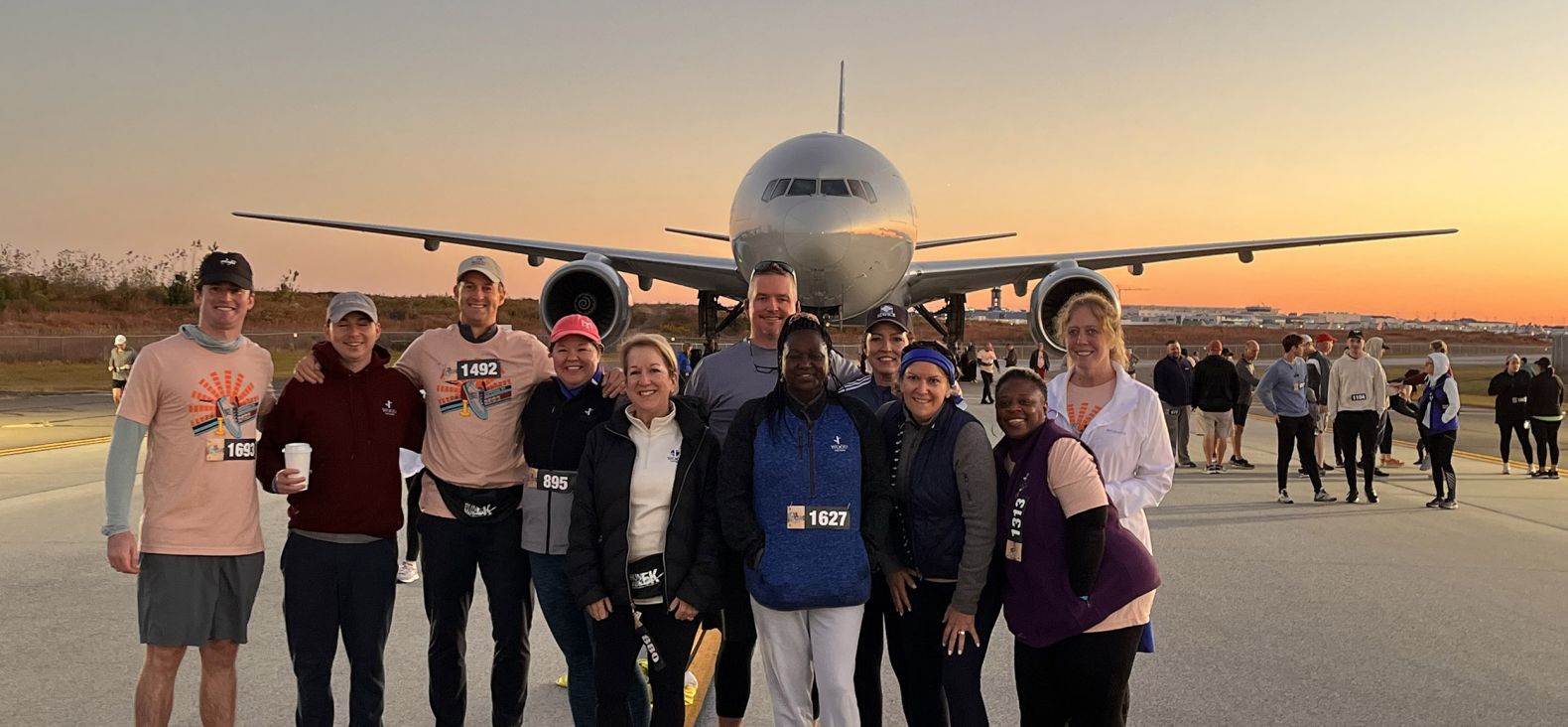 Group of co-workers standing in front of an airplane on a tarmac 