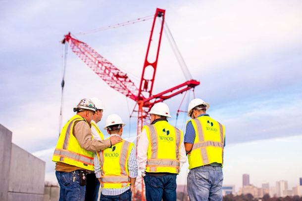 Group of construction workers look up a giant red crane structure