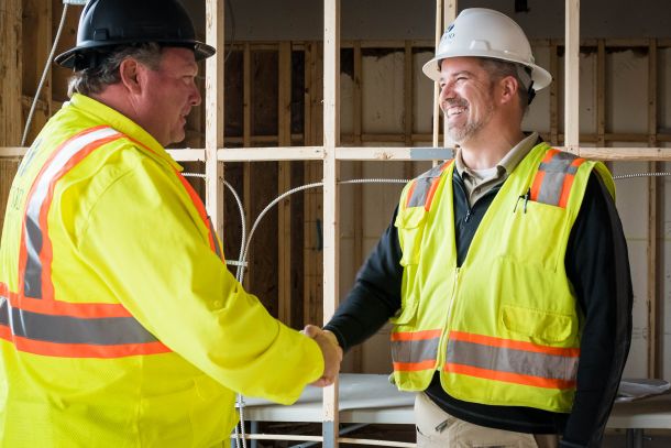 Two men in construction uniforms smile and shake hands