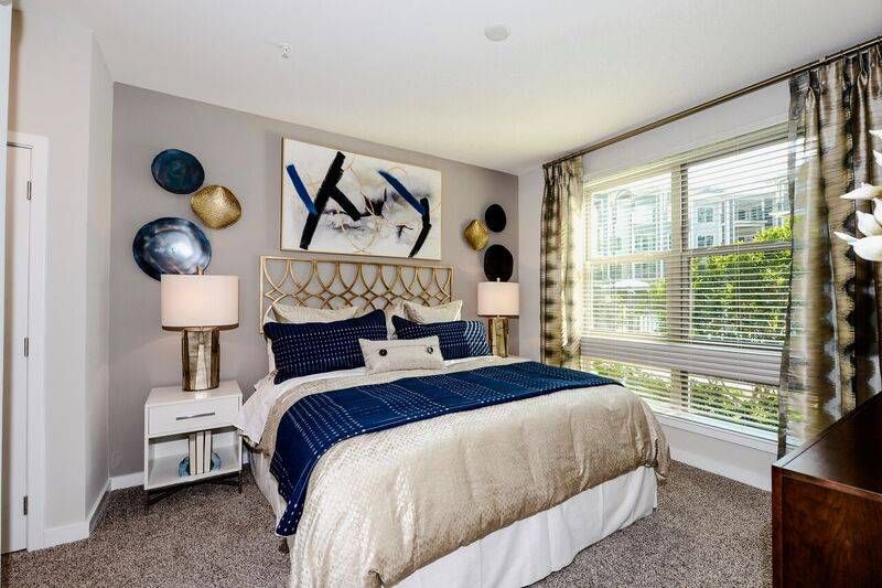 An elegantly decorated bedroom with a gold-accented bed frame, blue and white bedding, and art-adorned walls at Alta at Jonquil.